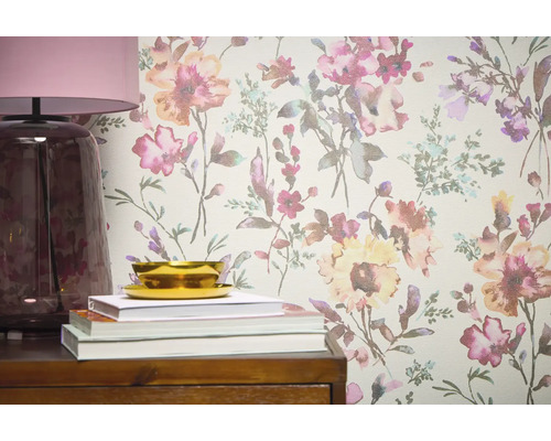 Close-up van een wand met bloemenbehang, aangevuld met een lamp, boeken en een schaal op een houten meubelstuk.