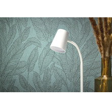 Close-up van een gestructureerd behang met bladmotief, een witte lamp en een vaas met decoratief gras