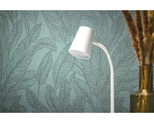 Close-up van een gestructureerd behang met bladmotief, een witte lamp en een vaas met decoratief gras