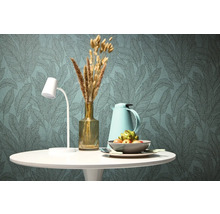 Decoratieve eettafel met lamp, thermoskan, vaas met droogbloemen en fruitschaal voor een behang met bladerpatroon