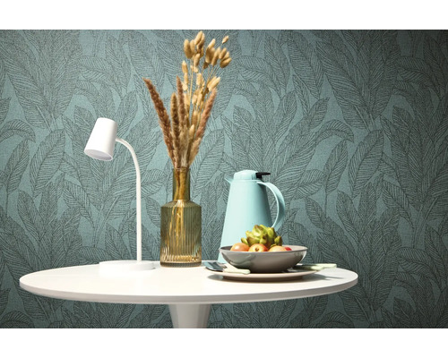 Decoratieve eettafel met lamp, thermoskan, vaas met droogbloemen en fruitschaal voor een behang met bladerpatroon