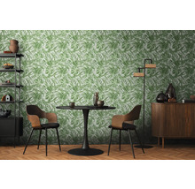 Woonkamer met eettafel, stoelen, rek, kast en een behang met plantmotief.