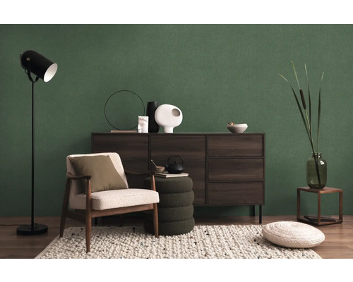 Woonkamer met fauteuil, staande lamp, dressoir en decoraties voor een groene wand