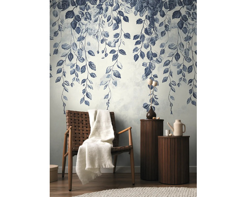 Decoratieve muur met bladerpatroon, fauteuil met deken en bijzettafels in de woonkamer.