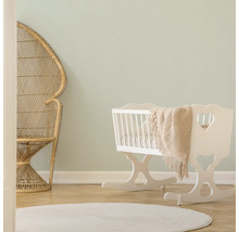 Lichte kamer met rotan stoel, witte wieg en rond vloerkleed.