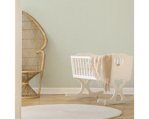 Lichte kamer met rotan stoel, witte wieg en rond vloerkleed.