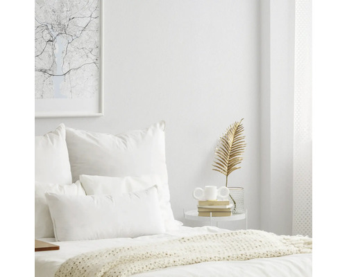 Lichte slaapkamer met bed, kussens, bijzettafel en decoratieve objecten