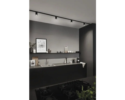 Moderne keuken met zwarte keukenkasten, spoelbak, plank en zwart railsysteem met spots.