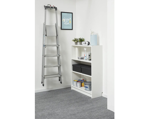 Zilveren aluminium trapladder aan een muurbeugel in een lichte, georganiseerde ruimte naast een wit rek.