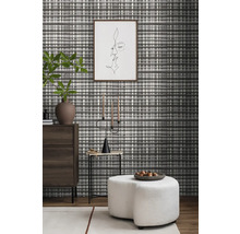 Woonkamer met patroonbehang, ladekast, bijzettafel, kandelaar en kruk.