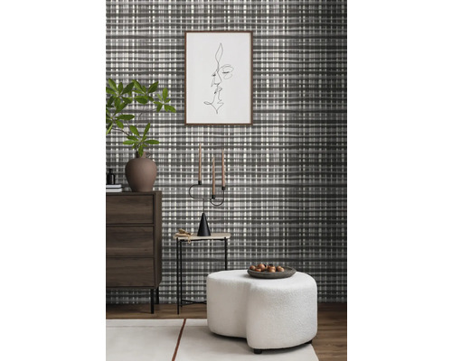 Woonkamer met patroonbehang, ladekast, bijzettafel, kandelaar en kruk.