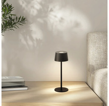 Zwarte tafellamp op een nachtkastje met boeken en een bed op de achtergrond