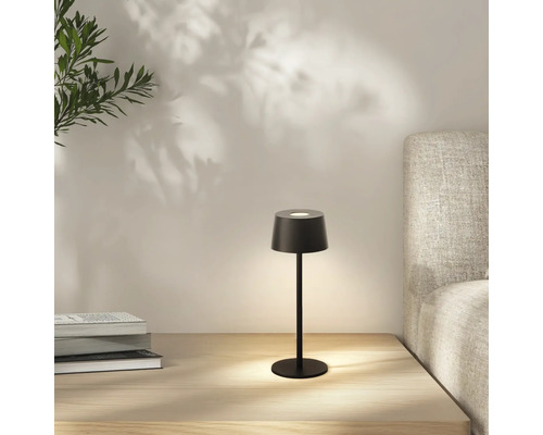 Zwarte tafellamp op een nachtkastje met boeken en een bed op de achtergrond