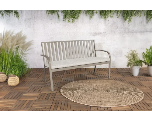 Metalen tuinbank met zitkussen op houten tegels en rond vloerkleed buiten.