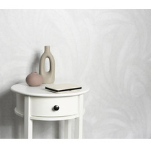 Licht behang met motief achter een wit nachtkastje met decoratie