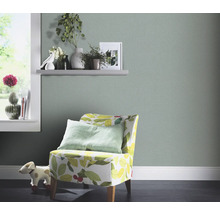 Woonkamer met lichtgroen behang, fauteuil met bladerdesign en decoraties op een plank