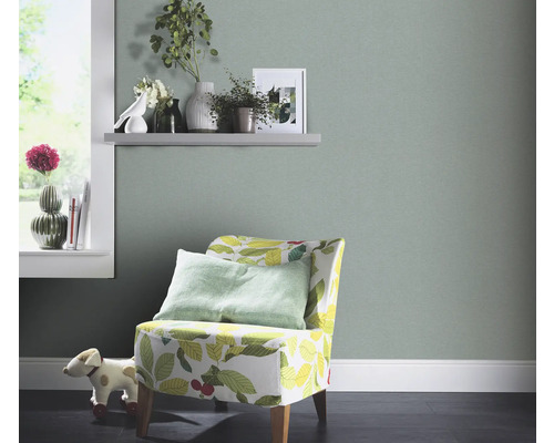 Woonkamer met lichtgroen behang, fauteuil met bladerdesign en decoraties op een plank