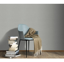 Scene met een stoel, een deken en een stapel boeken tegen een grijze muur.