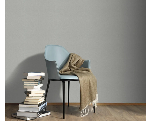 Scene met een stoel, een deken en een stapel boeken tegen een grijze muur.