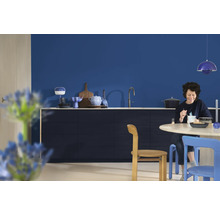 Lichte keuken met blauwe muur, eettafel, stoelen en een vrouw die aan het eten is