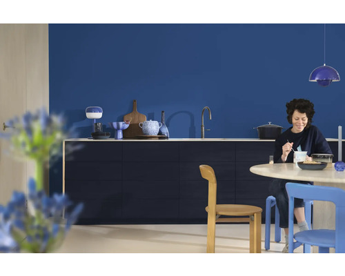Lichte keuken met blauwe muur, eettafel, stoelen en een vrouw die aan het eten is