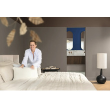 Lichte slaapkamer met bed en badkamer en suite, een vrouw maakt het bed op.