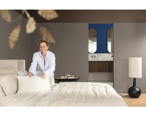 Lichte slaapkamer met bed en badkamer en suite, een vrouw maakt het bed op.