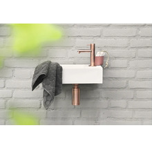 Kleine wastafel met kraan, handdoek en zeepdispenser aan een bakstenen muur