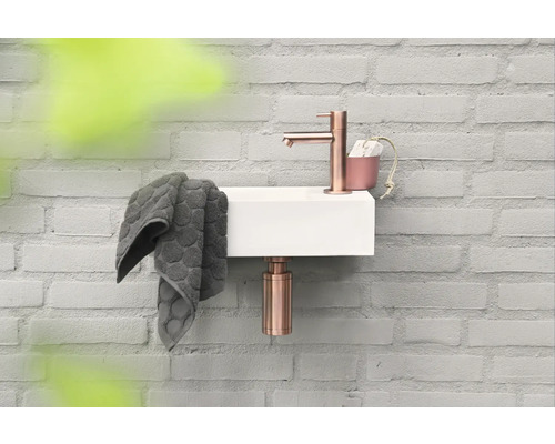 Kleine wastafel met kraan, handdoek en zeepdispenser aan een bakstenen muur