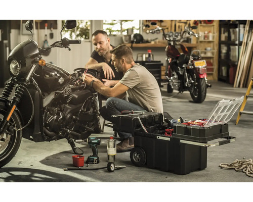 Twee mannen repareren een motorfiets met een gereedschapskist in een garage.