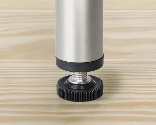 Detailopname van een verstelbare meubelpoot van metaal en kunststof op een houten oppervlak.