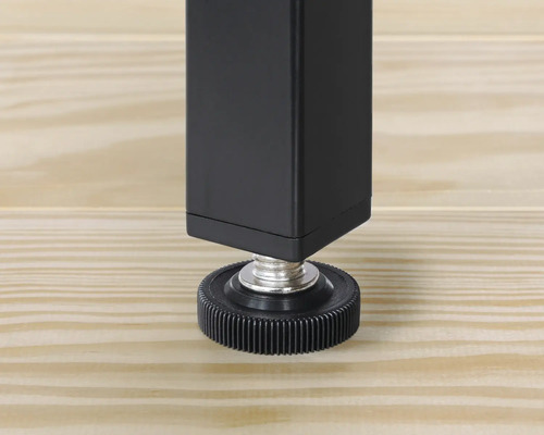 Detailopname van een zwarte tafelpoten met verstelbare voet op een houten vloer.