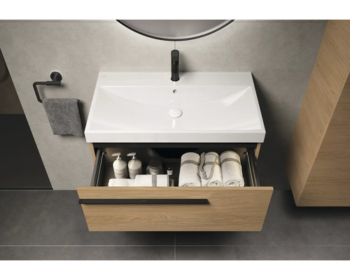 Wastafelonderkast met open lade, met handdoeken en verzorgingsproducten erin. Boven de wastafel hangt een spiegel.