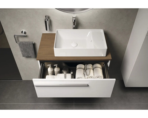 Moderne badkamer met witte waskom op houten blad en open lade-element gevuld met handdoeken en verzorgingsproducten.