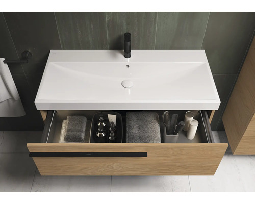 Wastafelonderkast met open lade, wastafel, kraan en badkamerartikelen.