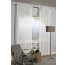 Scene met transparante gordijnen voor een raam, een fauteuil, een bijzettafel en een vloerlamp