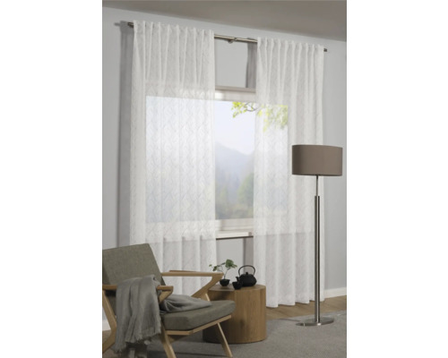 Scene met transparante gordijnen voor een raam, een fauteuil, een bijzettafel en een vloerlamp