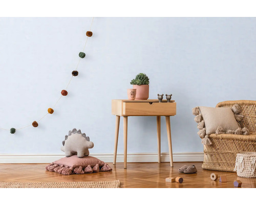 Lichte kinderkamer met houten vloer, houten tafel, rotan stoel en decoratieve elementen zoals een slinger, kussens en een plant.