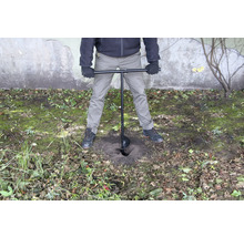 Een persoon gebruikt een grondboor om een gat in de grond te boren.