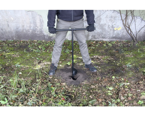 Een persoon gebruikt een grondboor om een gat in de grond te boren.