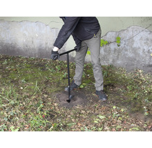 Een persoon boort een gat in de grond met een grondboor.