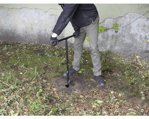 Een persoon boort een gat in de grond met een grondboor.