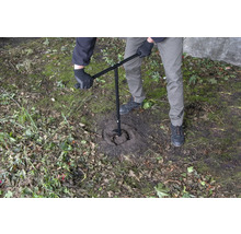 Een persoon gebruikt een grondboor om een gat in de grond te boren.