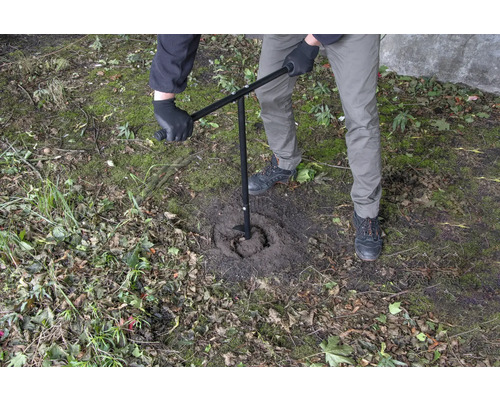 Een persoon gebruikt een grondboor om een gat in de grond te boren.