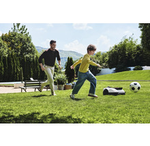 Man en kind spelen voetbal met robotmaaier in de tuin.