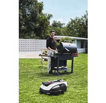 Man aan het barbecueën in de tuin met een barbecue en een robotmaaier.