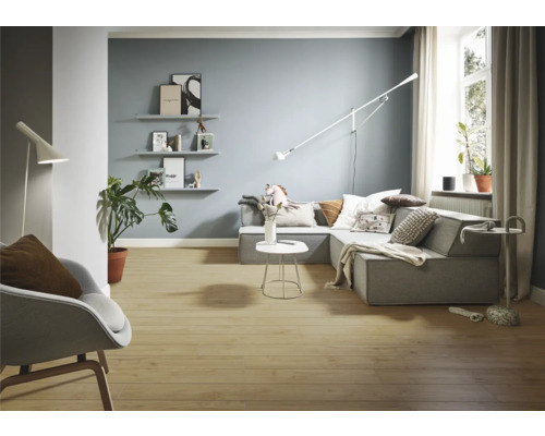 Woonkamer met grijze hoekbank, staande lamp en houten vloer