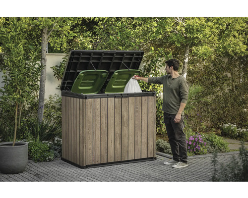 Houten afvalcontainerbox met twee groene afvalcontainers en een persoon die een afvalzak erin gooit