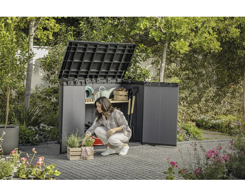 Tuin met een vrouw die knielt voor een open gereedschapskast waarin tuingereedschap wordt opgeborgen.