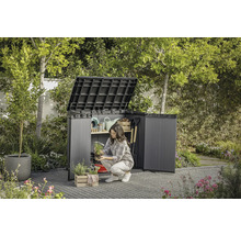 Tuinscene met open gereedschapskast waarin een vrouw tuingereedschap opbergt.